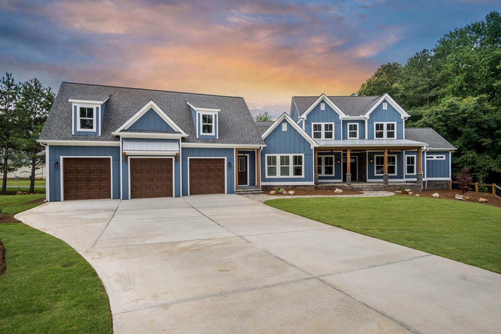 Blue custom home with wooden garage doors beneath a sunset sky
